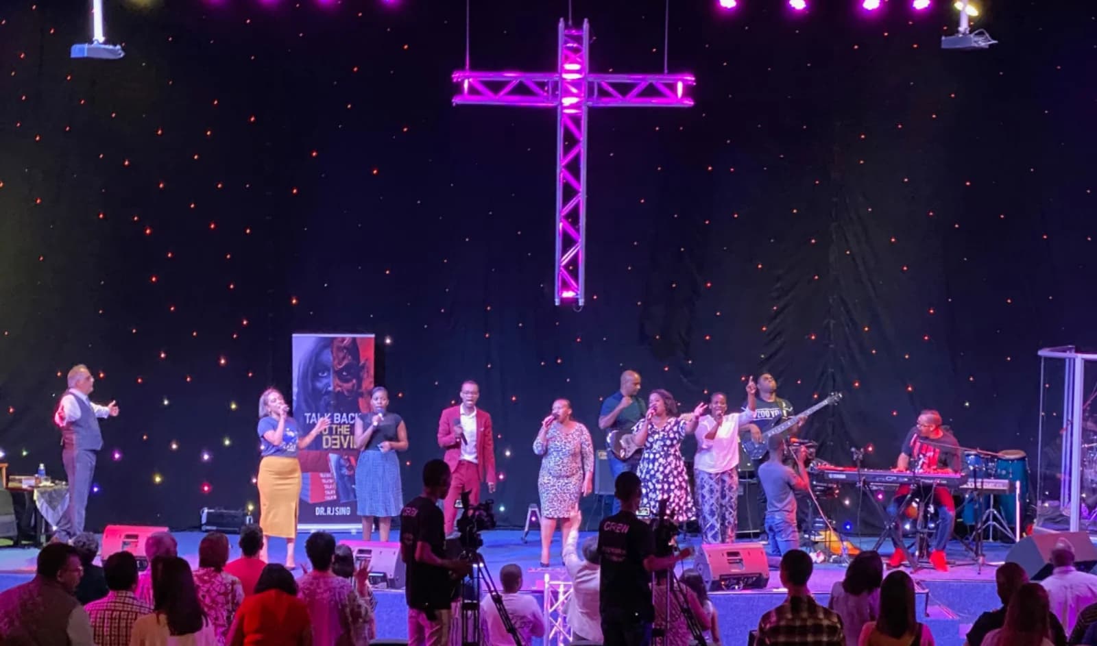 The worship team leading a Sunday service at FCI, beneath a lit cross